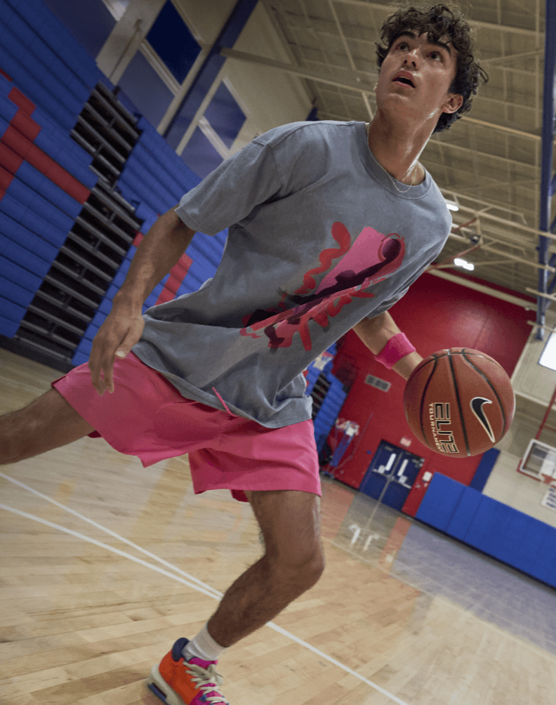 Person dribbling a basketball on an indoor court while wearing athletic clothing and colorful basketball shoes.