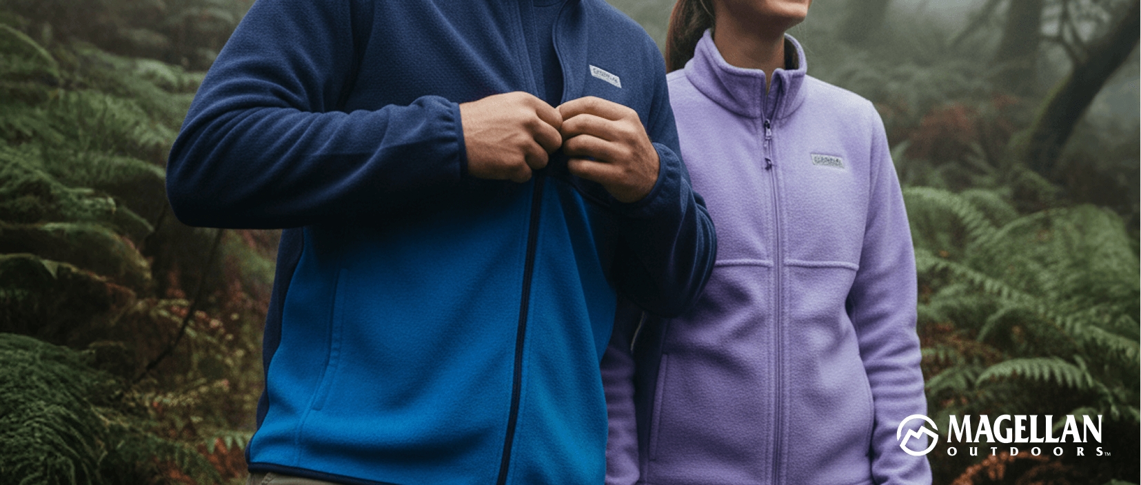 Two people wearing Magellan Outdoors zip-up fleece jackets in blue and light purple, standing in a green outdoor setting with ferns.