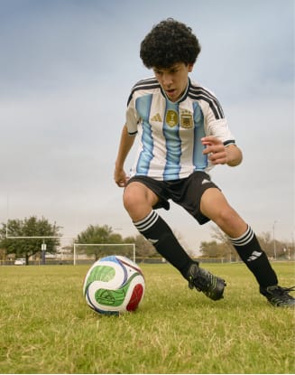 Person dribbling a soccer ball on a grass field while wearing a striped soccer jersey.