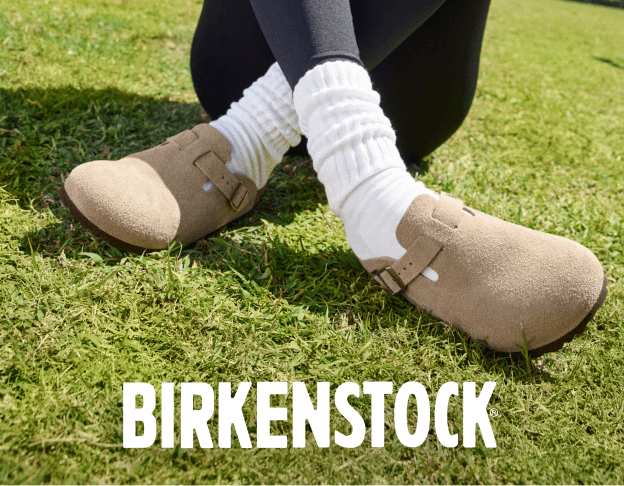 Feet wearing Birkenstock clogs with socks on grass.