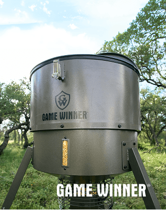 Game Winner deer feeder in outdoor wooded setting.