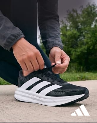 Close-up of hands tying the laces of a black adidas Galaxy 8 running shoe on an outdoor path.