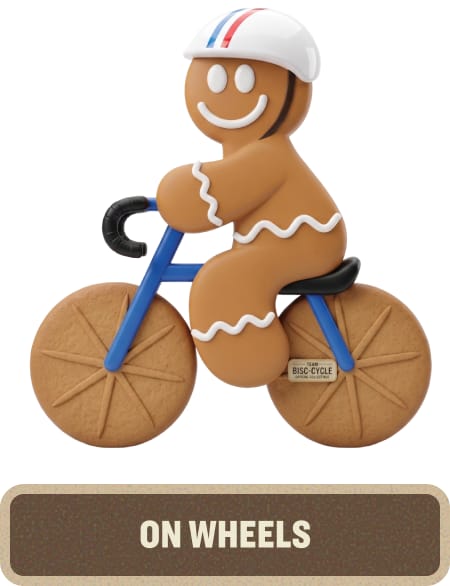 Gingerbread character riding a blue bicycle while wearing a cycling helmet. Text below reads “On Wheels.”