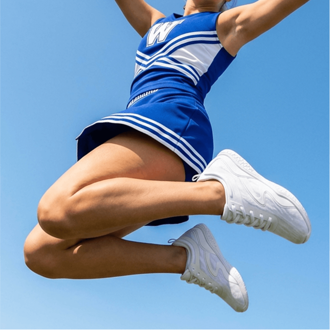 Athlete mid-air wearing a blue cheer uniform and white shoes against a clear sky.