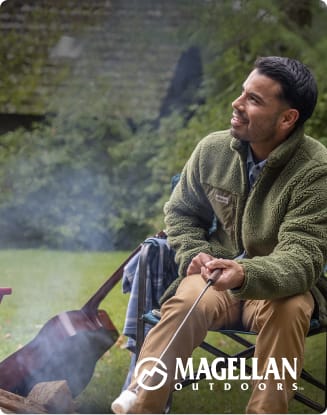 Person wearing a green Magellan Outdoors fleece jacket while seated outdoors near a campfire.