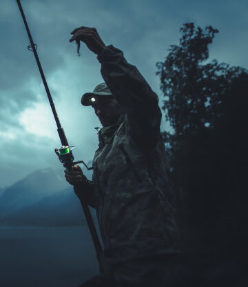 A male angler night fishing with a rod by a lake.