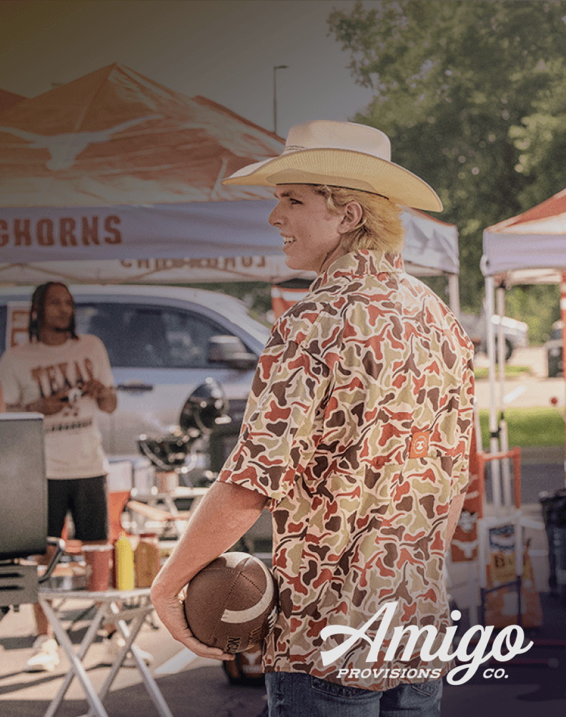 Person holding a football while wearing a camouflage-pattern button-down shirt at an outdoor tailgate event.