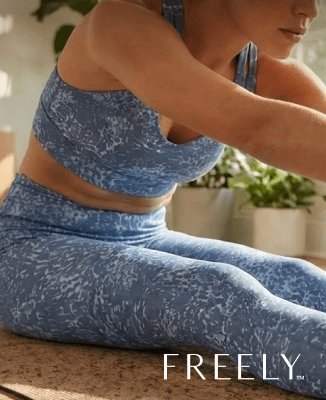 Person wearing blue patterned Freely activewear set while stretching indoors near plants.