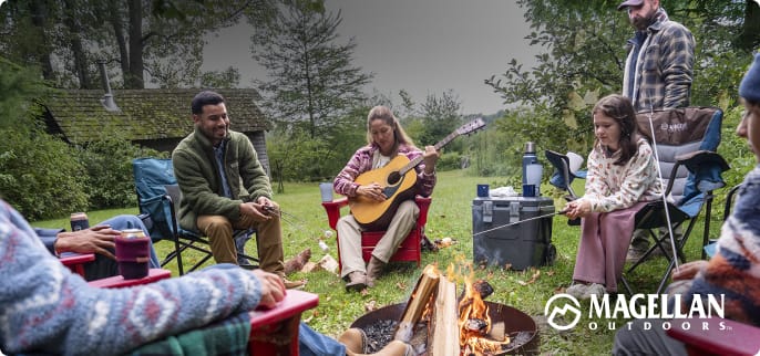 Person sitting in a camp chair near a campfire roasting a marshmallow at an outdoor campsite.