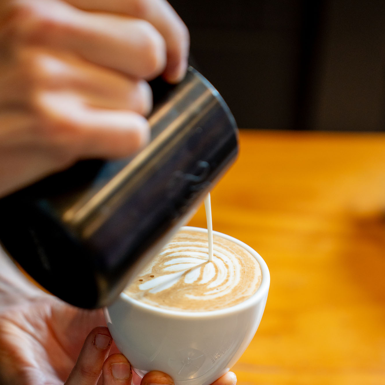 A close-up photo of a takeaway coffee cup with a lid, shot in a warm, cozy café setting. The image conveys a casual coffee break vibe suitable for a blog or promotional content about coffee or a coffee flight.