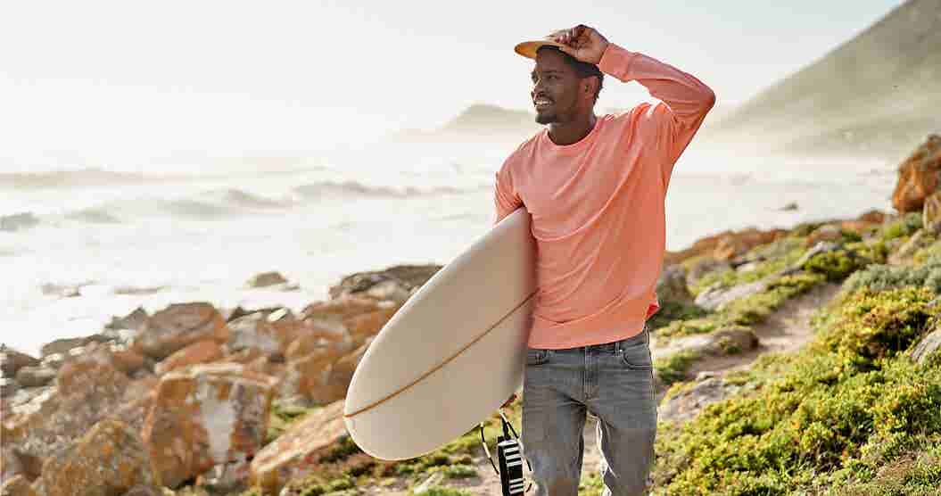 Man holding surfboard while looking out over the ocean.