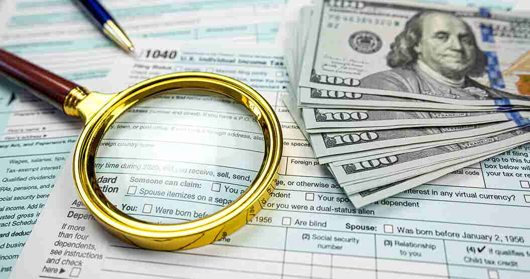 a magnifying glass and money sitting on top of IRS tax forms