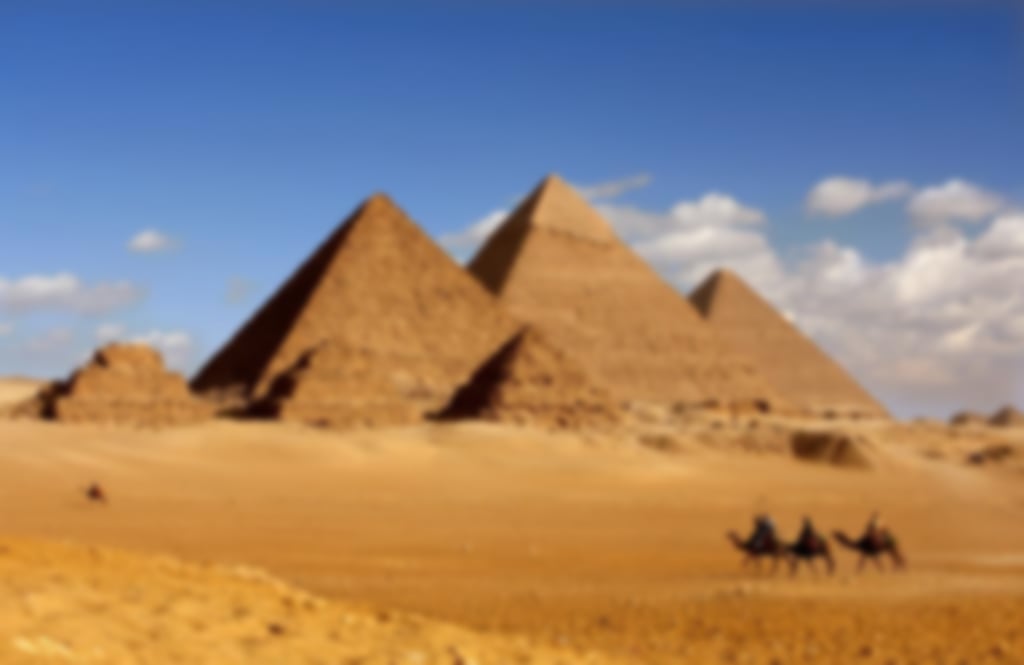 A view of five Egyptian pyramids with camels riding in the foreground