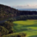 Downward view of the fairway and green at Wild Coast. The river to the left of the hole guards the green as well as the sea in the background.