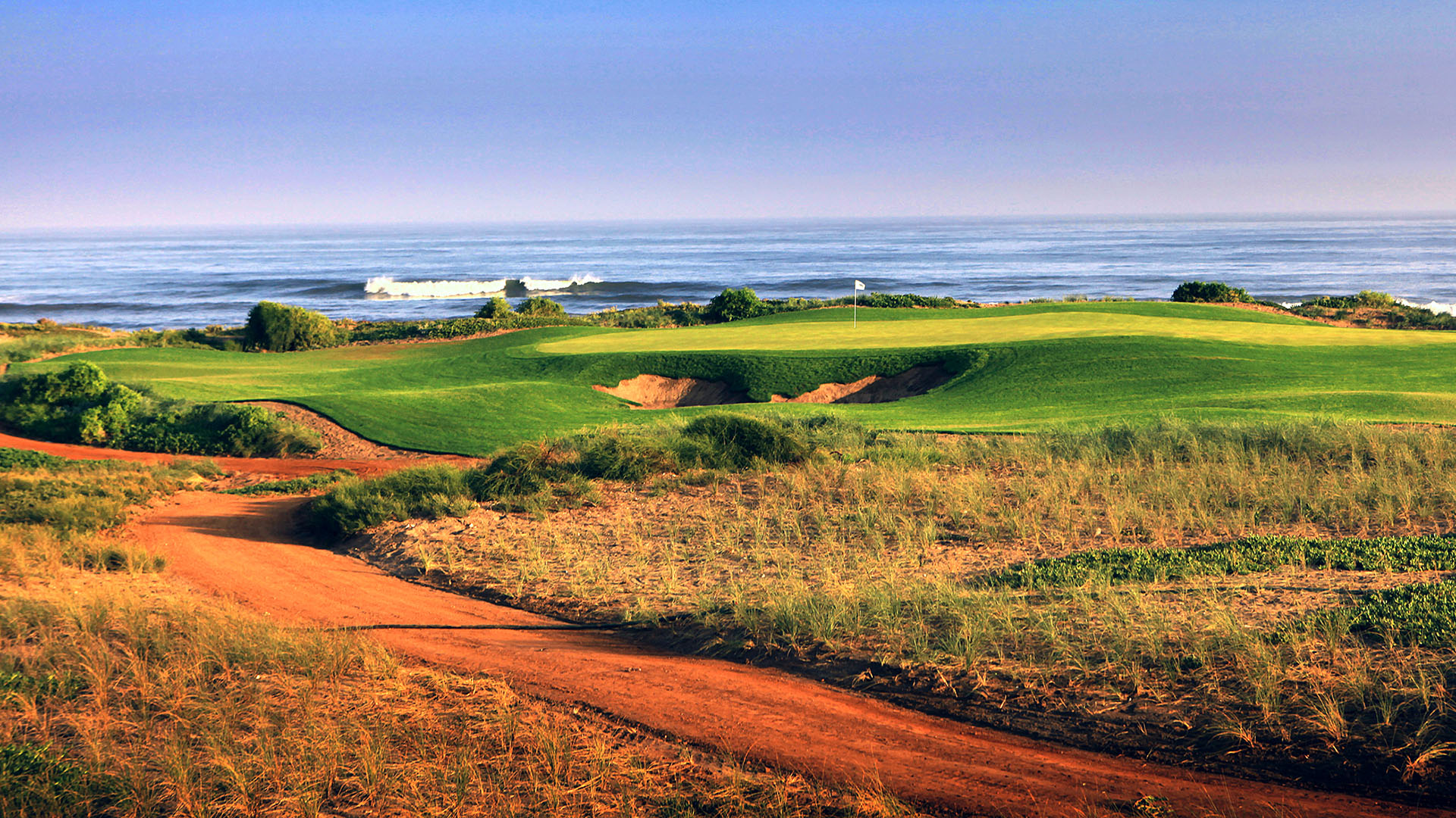 Orange sand with lush green fairways and greens, overlooking the sea.