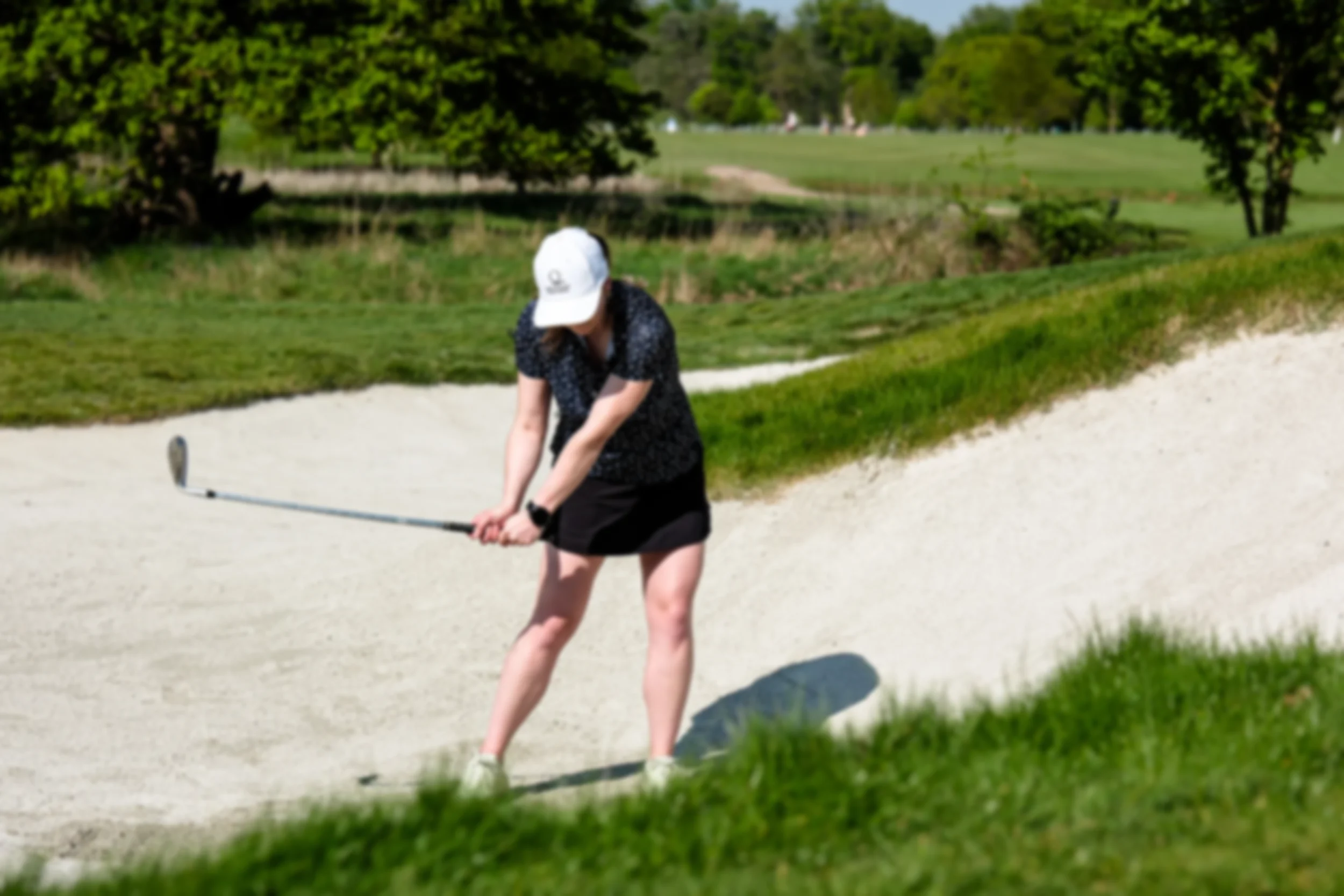 Golfer executing a bunker shot at Royal Ascot Golf Course under clear blue skies.
