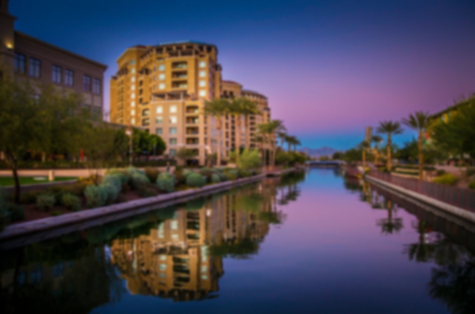 Twilight view of Scottsdale with buildings and palm trees reflecting in a canal.