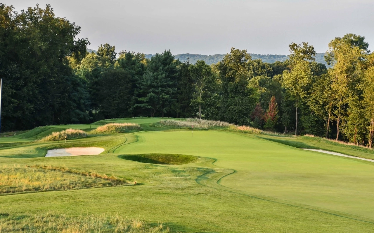 a well-maintained golf course , surrounded by trees and greenery, featuring a large green.