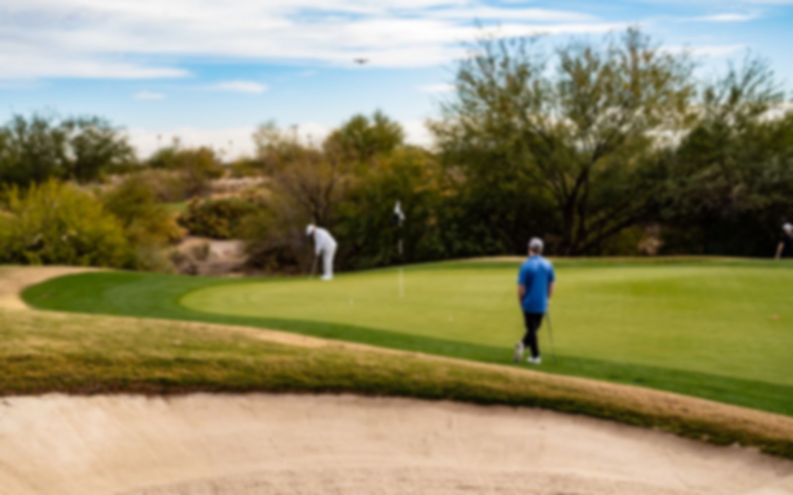 Two golfers on the green with a sand bunker in the foreground.