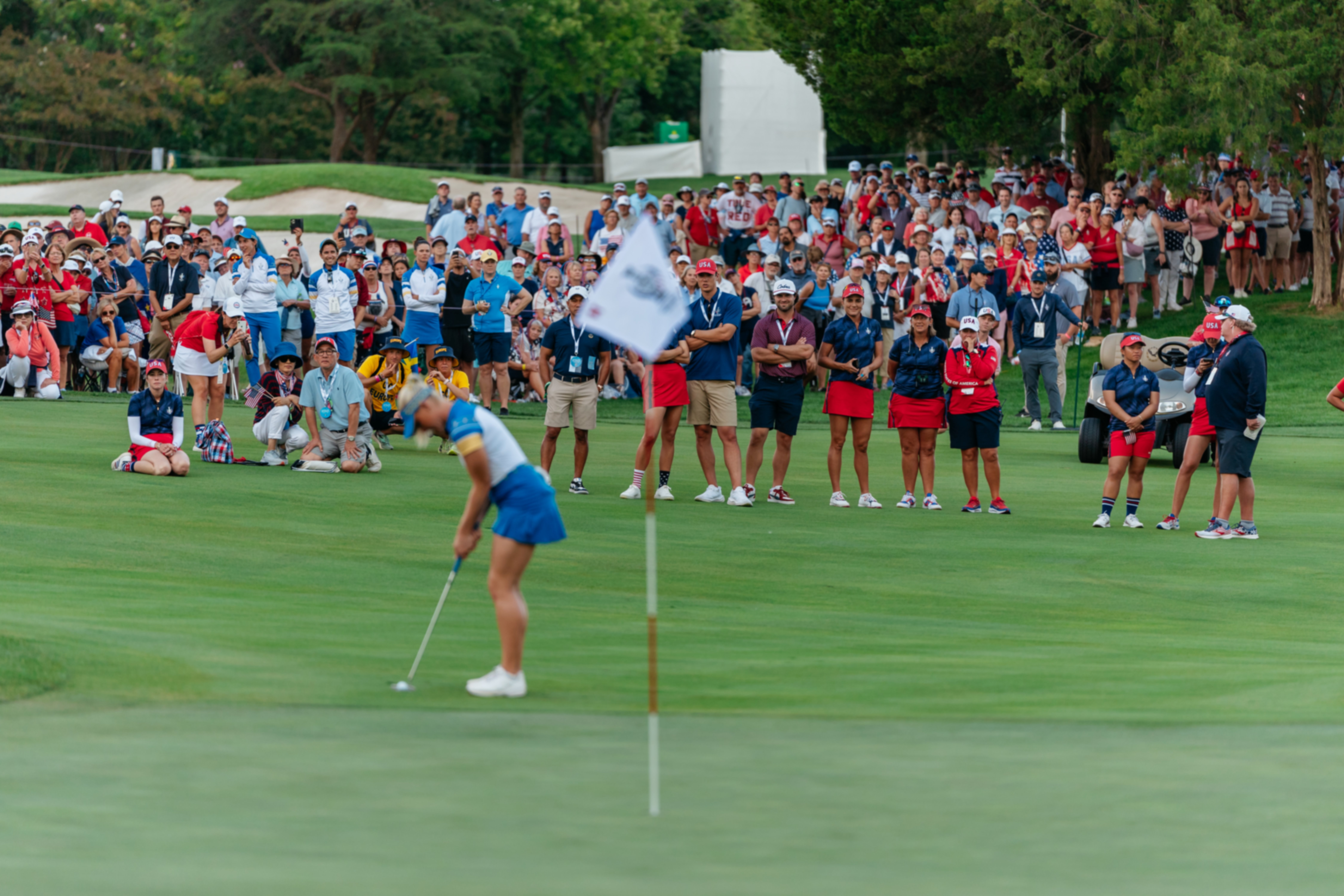 The USA team and fans watching a european player set up to hit a shot next to the green