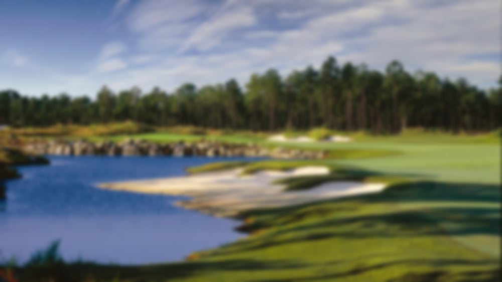 Tree-lined background with bunkers and a water hazard on the left of the hole.