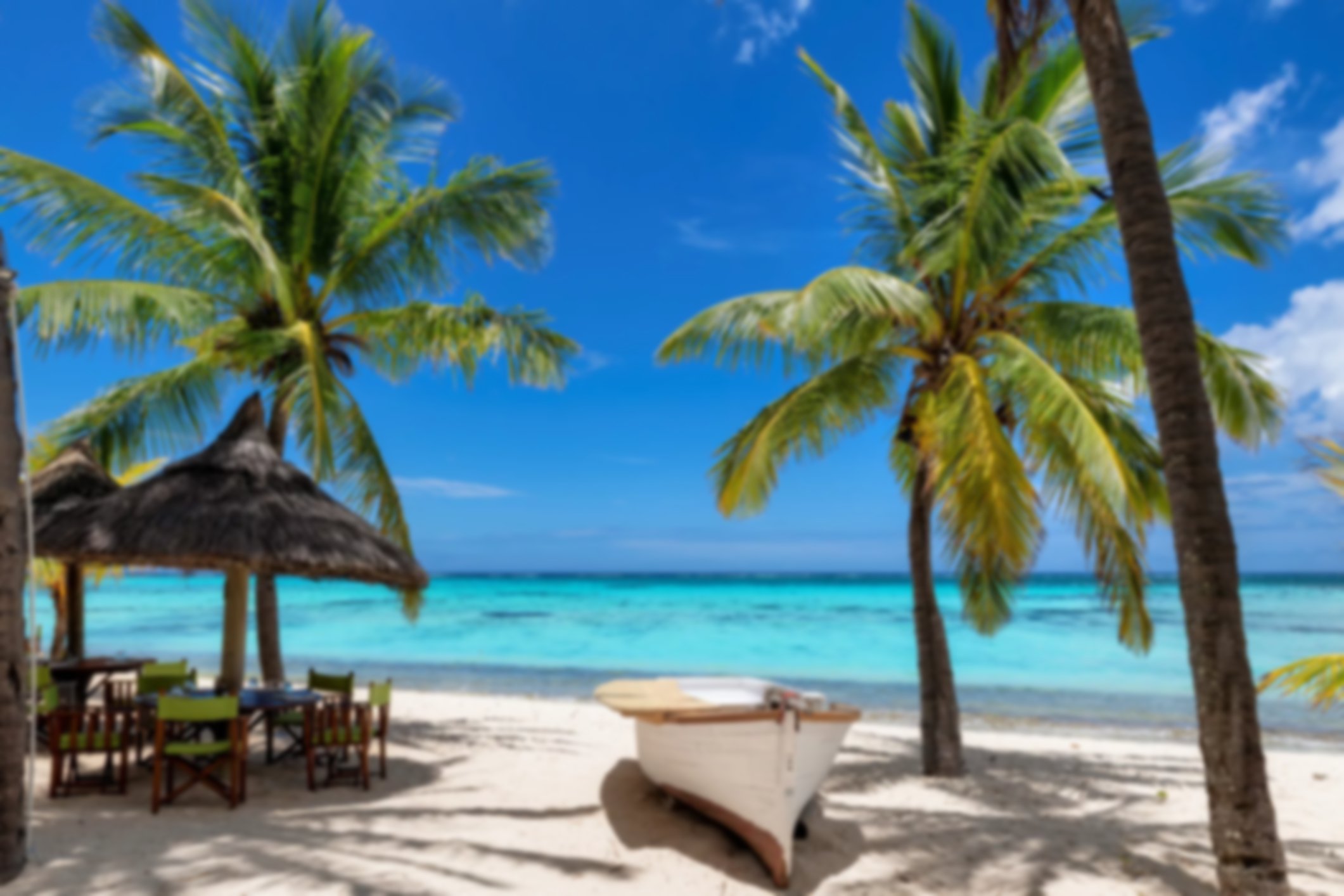 Beach cafe on sandy beach under straw umbrella, palm trees and beautiful sea on exotic tropical island.