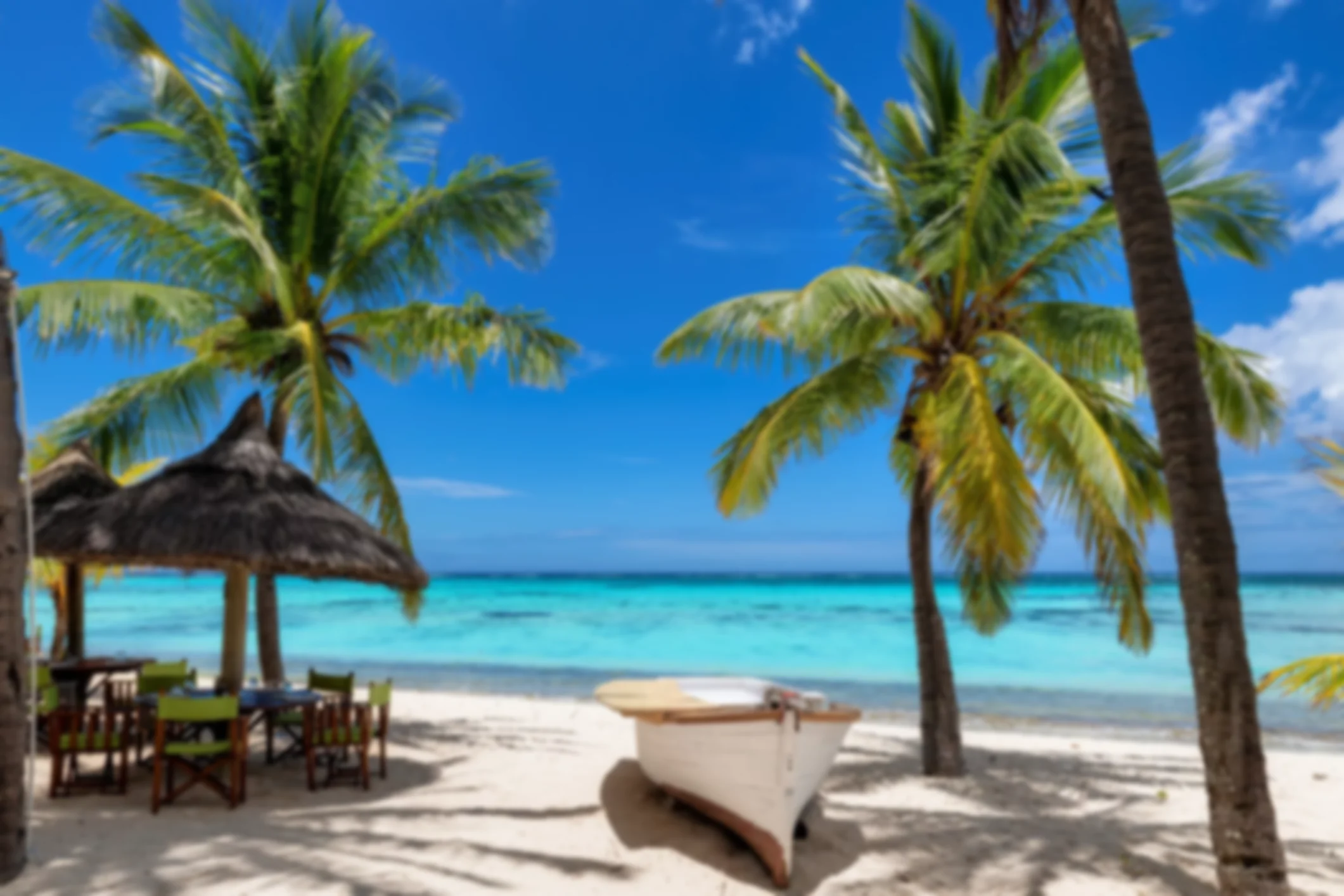 Beach cafe on sandy beach under straw umbrella, palm trees and beautiful sea on exotic tropical island.