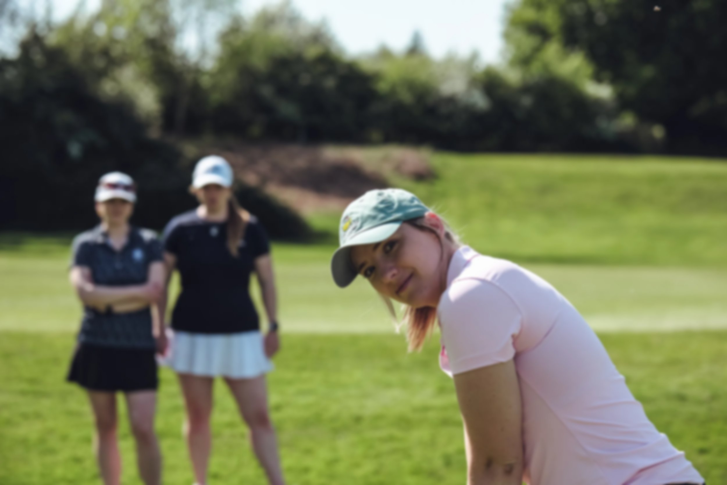 Golfer preparing her golf stance in the foreground, with two golfers standing behind at the Royal Ascot course.