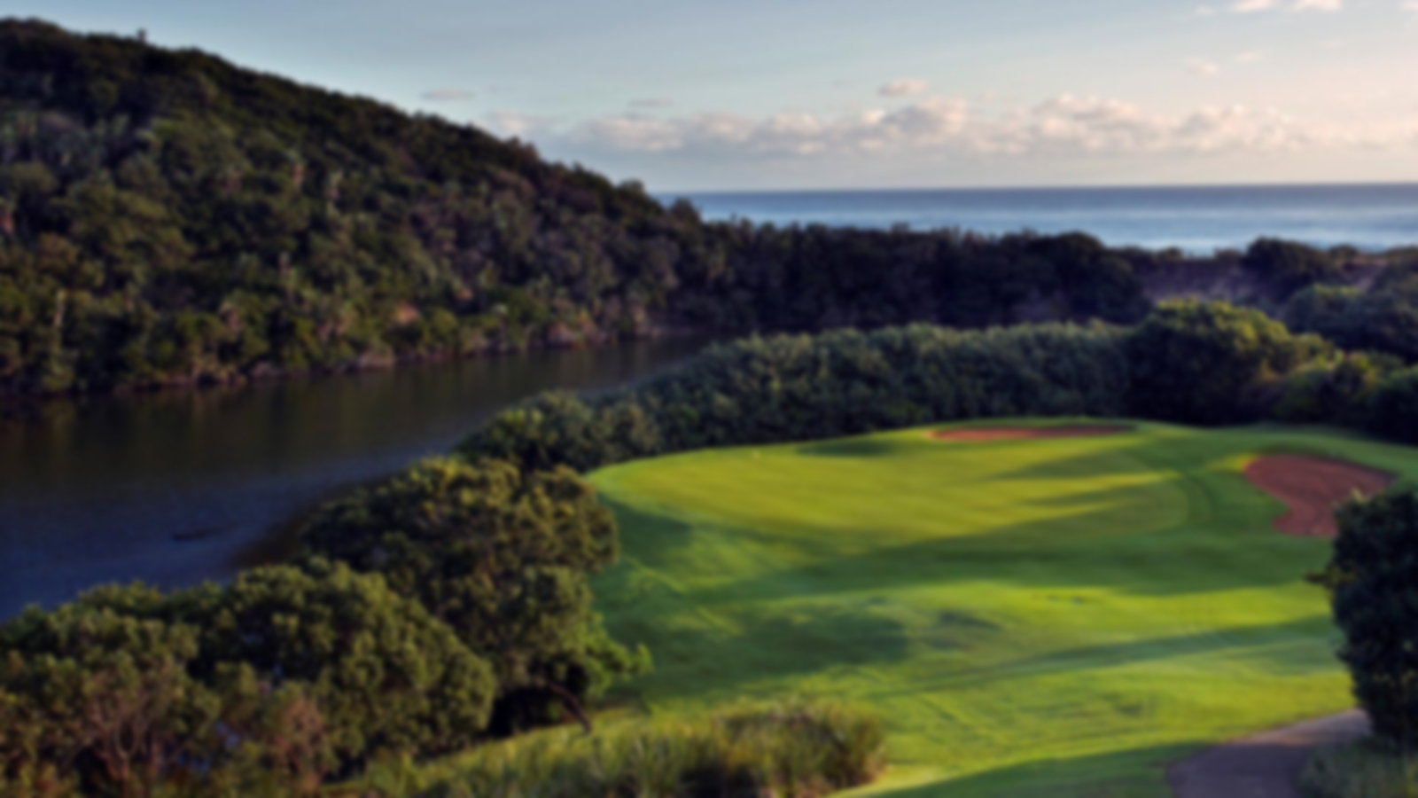 Downward view of the fairway and green at Wild Coast. The river to the left of the hole guards the green as well as the sea in the background.