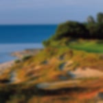Tight fairway with bunkers on the side of a hill leading down to the ocean.