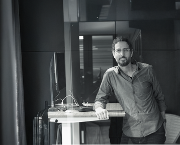 a man with glasses leaning on a desk in an office