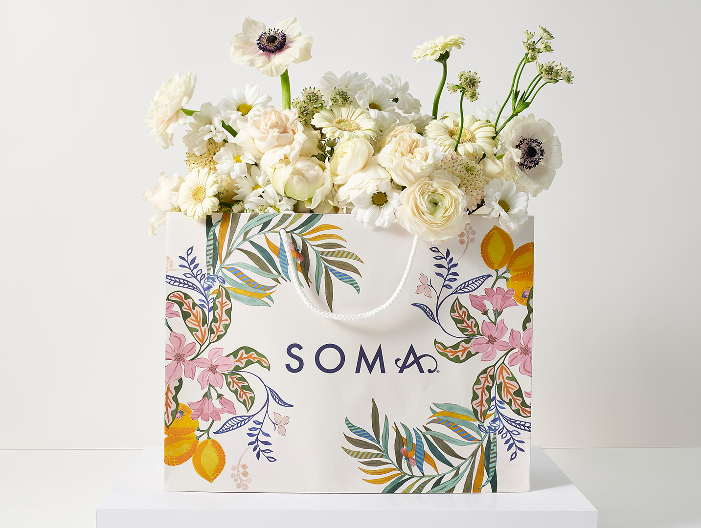 White floral stems displayed in a floral and lemon printed Soma<sup class=st-superscript>®</sup> shopping bag.