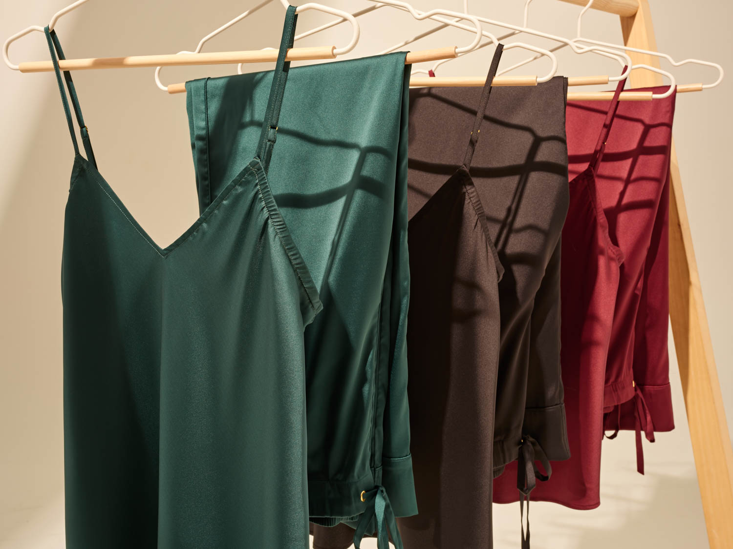 Soma<sup class=st-superscript>®</sup> satin pajama separates in dark green, black, and burgundy hanging in a row on a rack.
