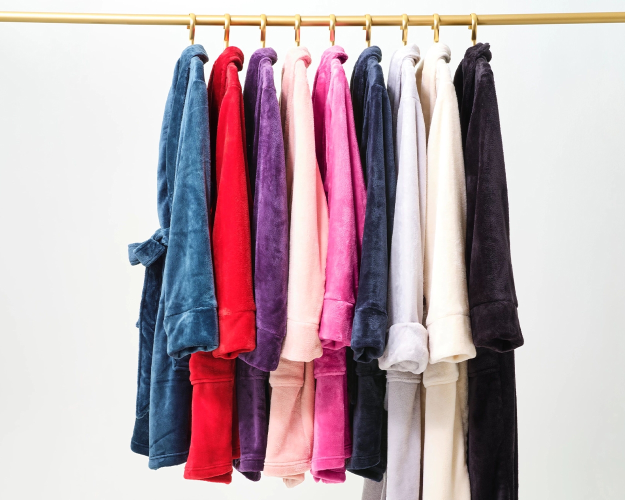 Soma<sup class=st-superscript>®</sup> blue, red, purple, light pink, pink, navy, grey, off-white, and black plush robes hanging in a row on a clothing rack.