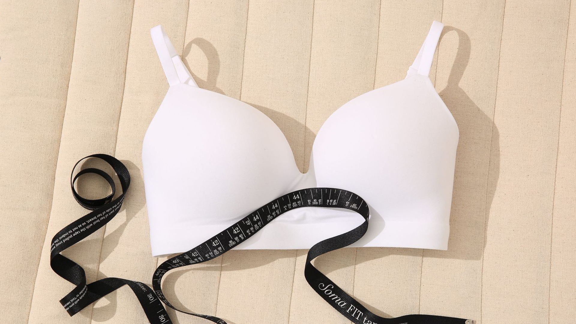 Soma<sup class=st-superscript>®</sup> laydown of white wireless bra and black measuring tape.