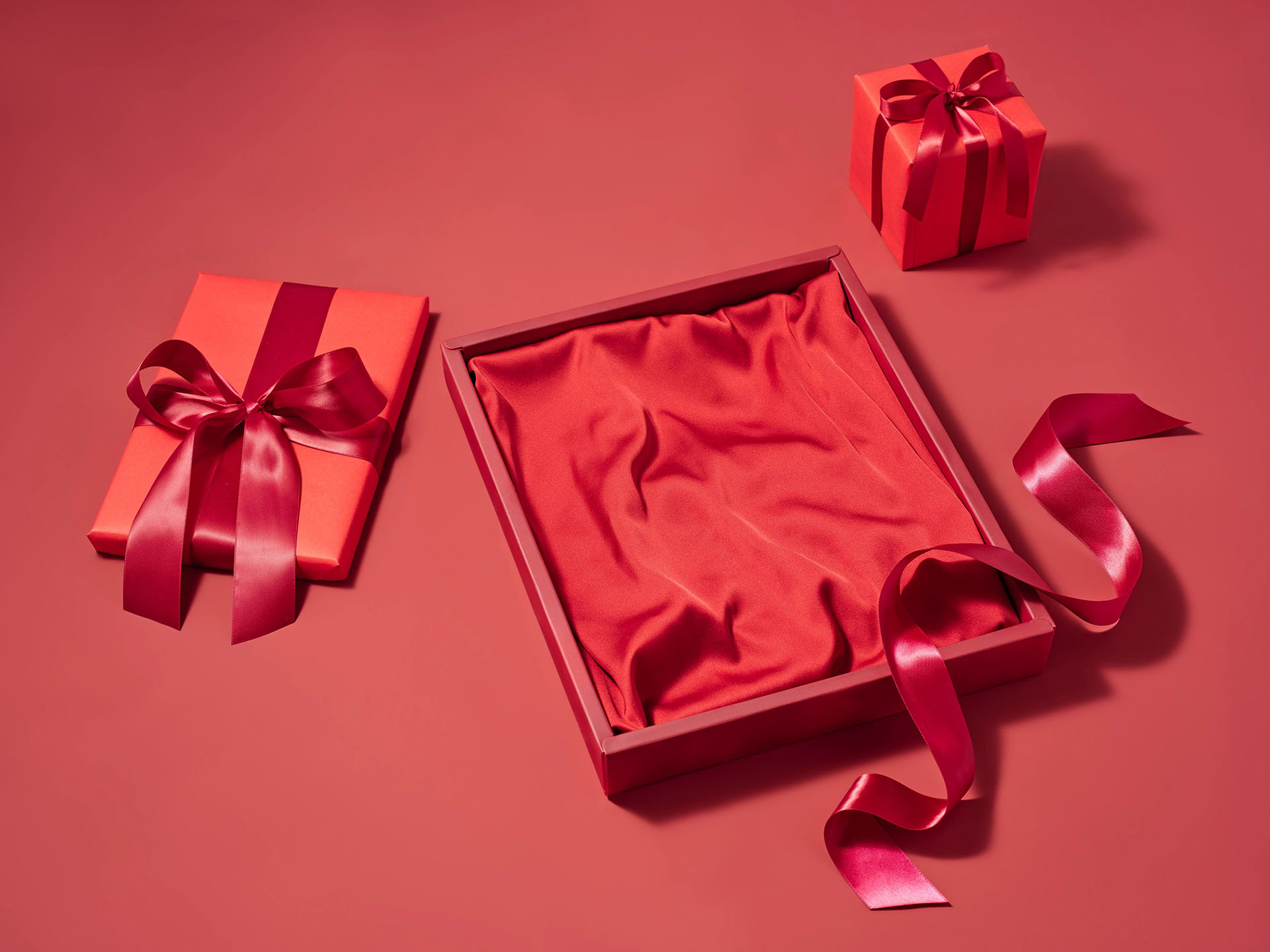  Laydown of an empty red gift box with loose red ribbon and two red packaged gift boxes with red ribbon bows.