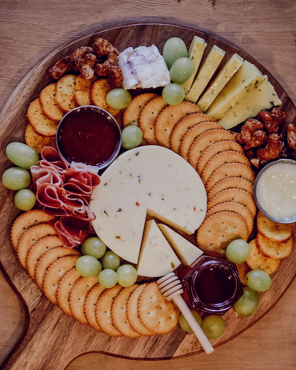 ood cheese board with sliced cheese, meat, crackers, nuts, fruit, and sauces.