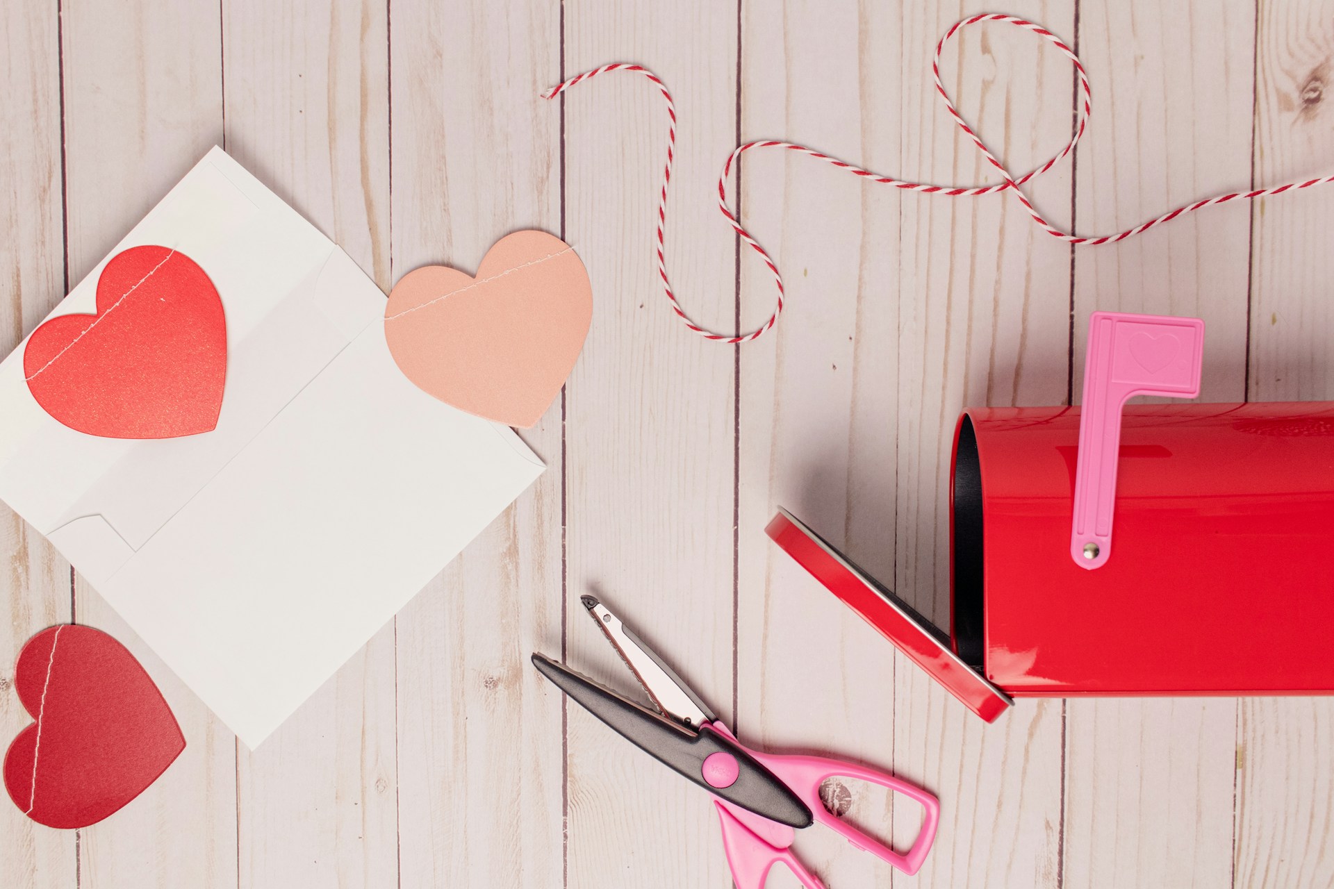 Valentine's Day craft of paper hearts, scissors, string, and a mailbox.