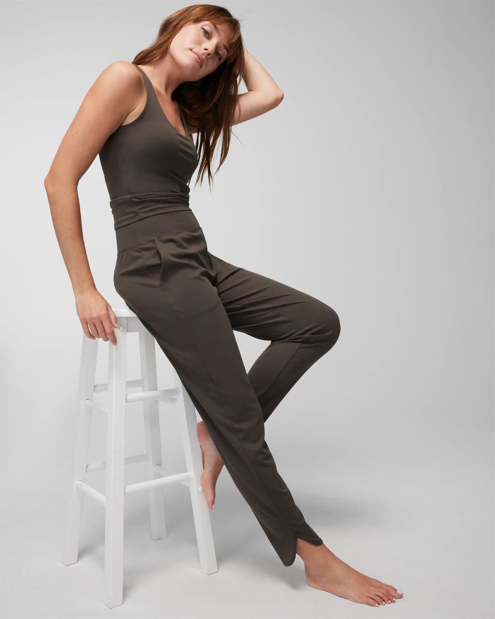 Soma<sup class=st-superscript>®</sup> model sitting on a stool, wearing dark grey olive tank top and jogger leggings. 