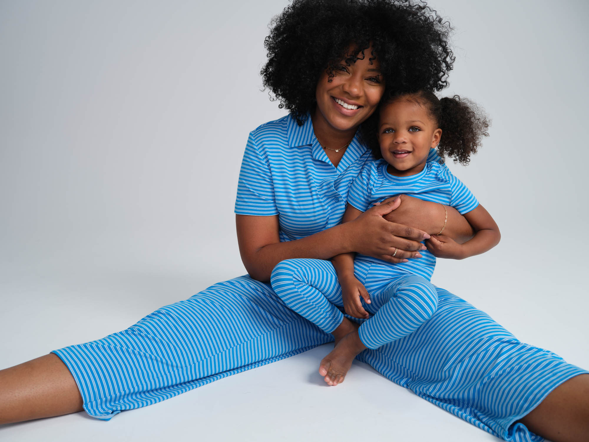 Soma women's model sitting with her daughter wearing blue striped matching  mommy and me pajamas for Mother's day.