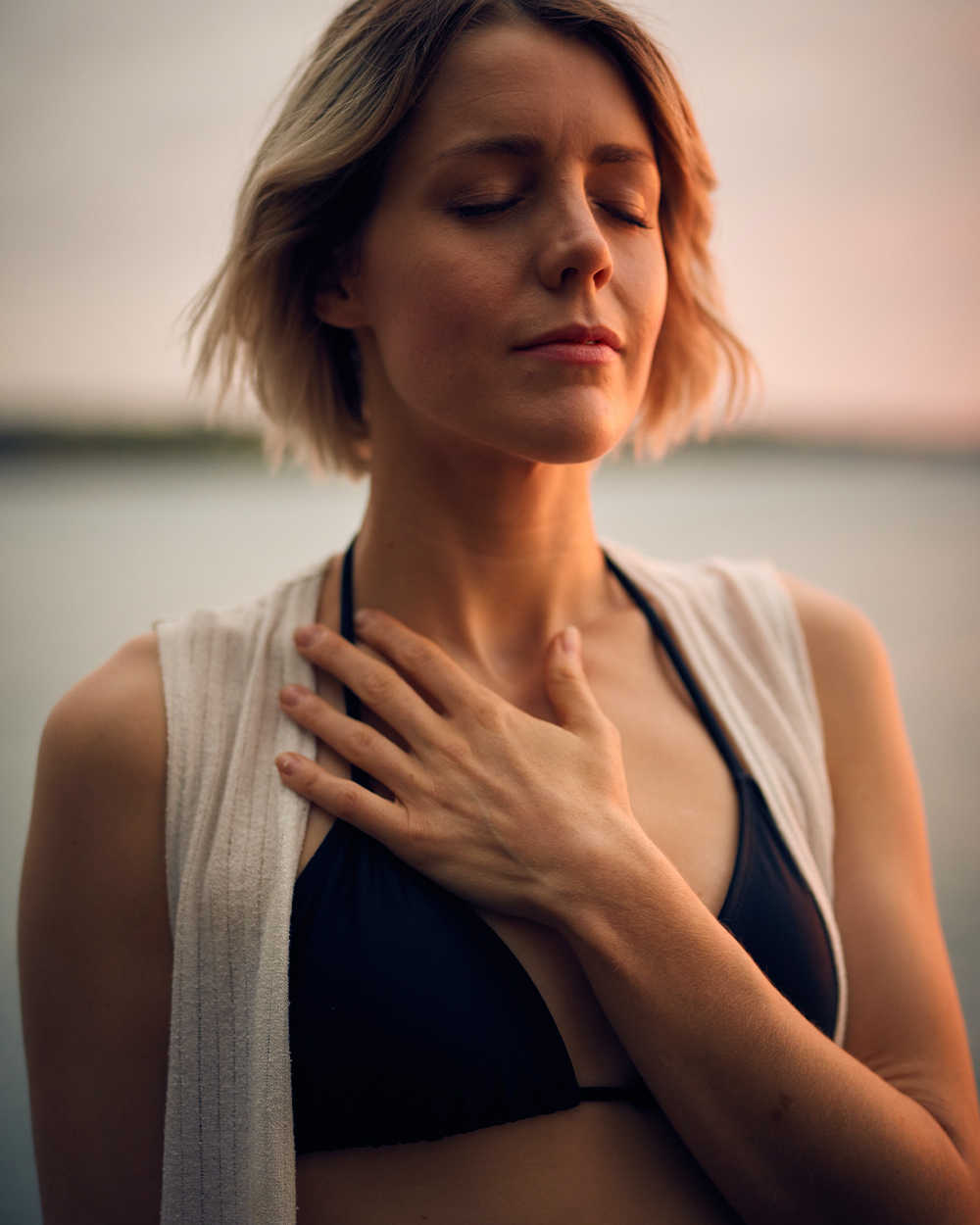 Model standing with her eyes closed and her hand on her chest.