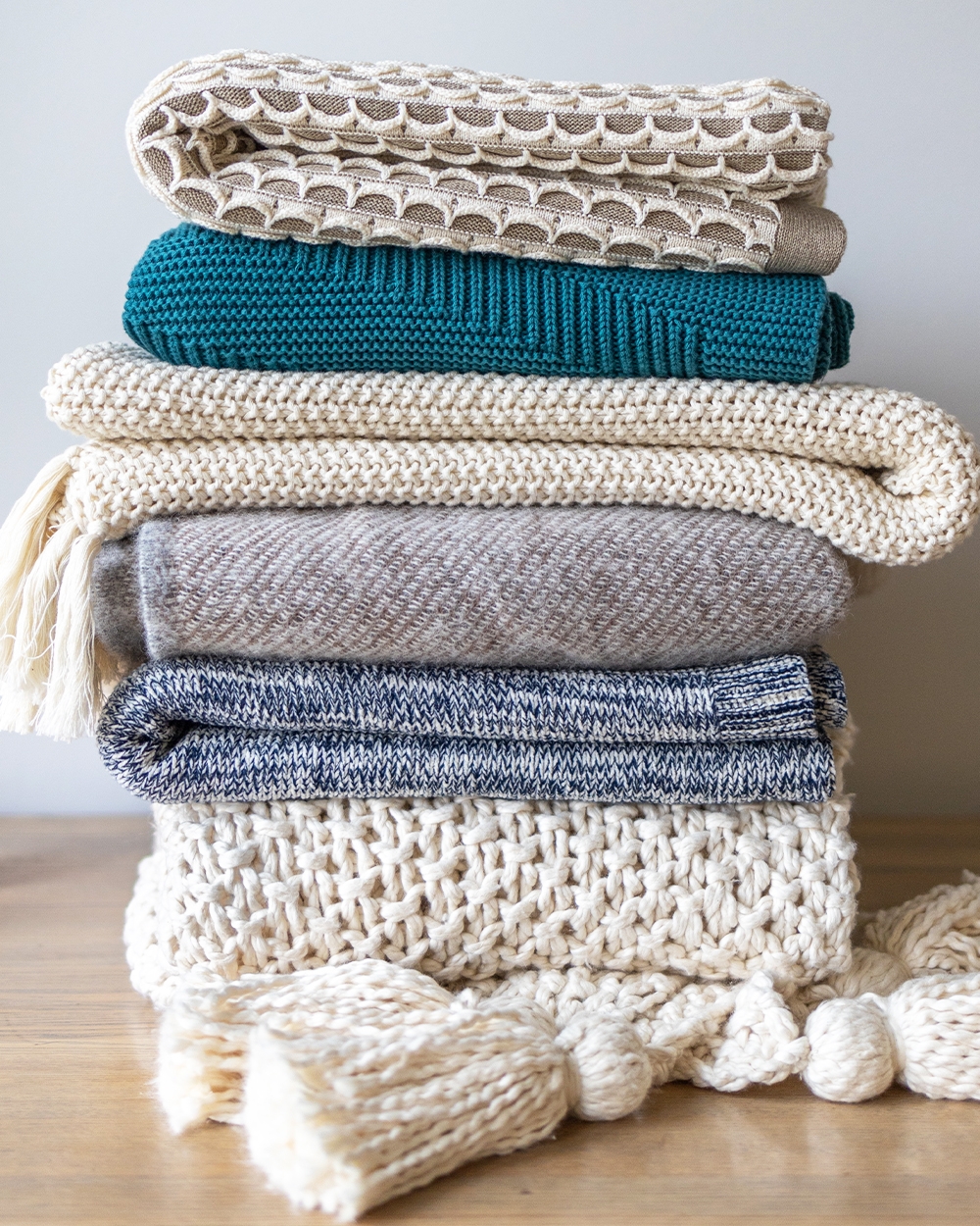 Stack of knit blankets in a variety of weights in beige, grey, and blue hues.