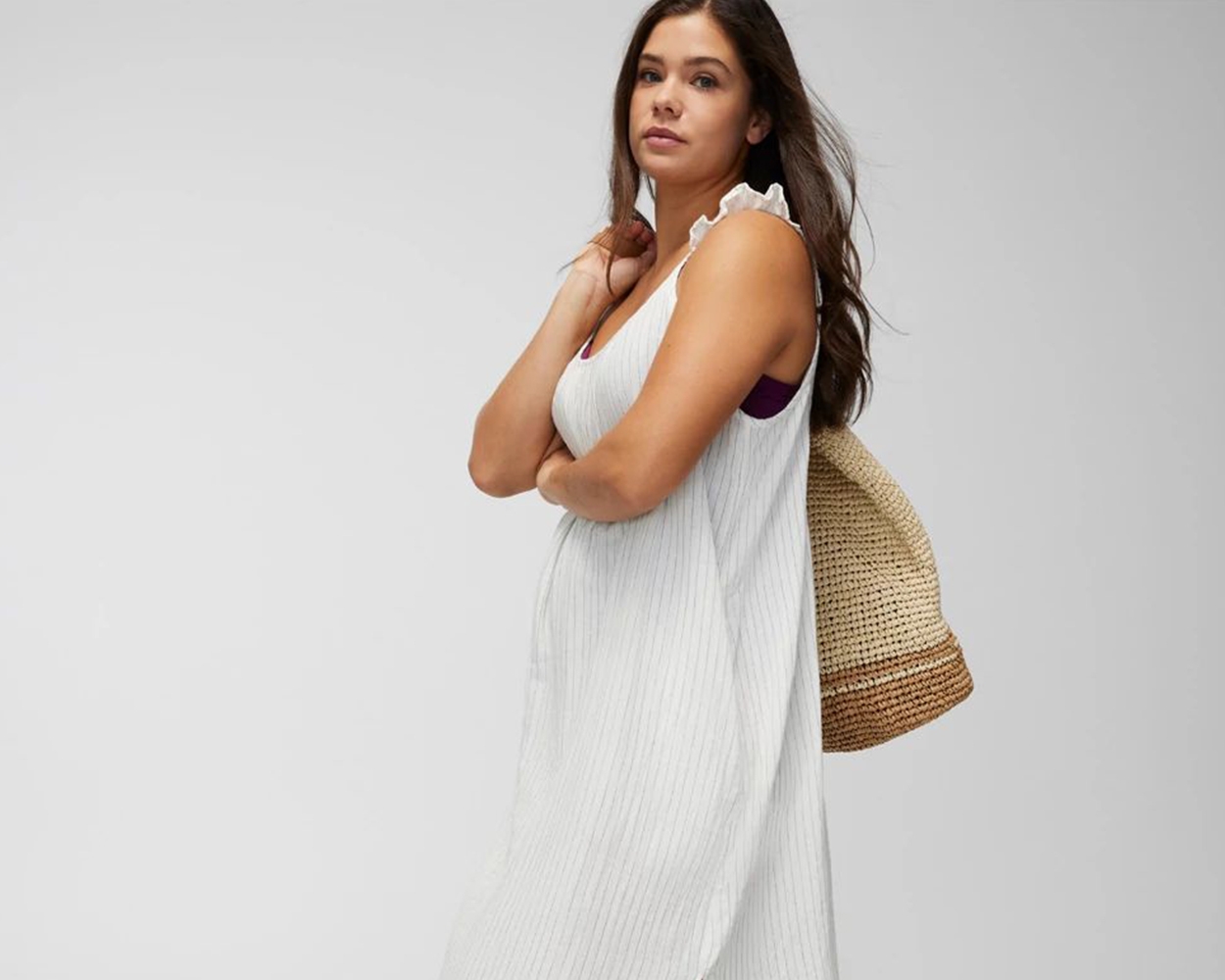 Soma<sup class=st-superscript>®</sup> model wearing a sleeveless white swim cover-up dress, carrying a tan oversized beach bag.