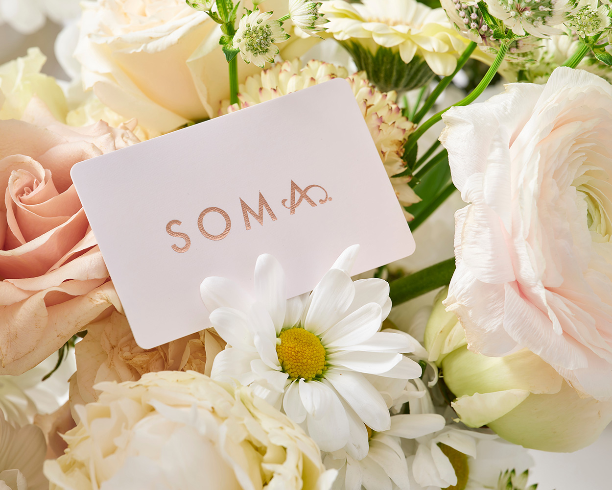 Soma<sup class=st-superscript>®</sup> gift card sitting on a white and blush floral bouquet.
