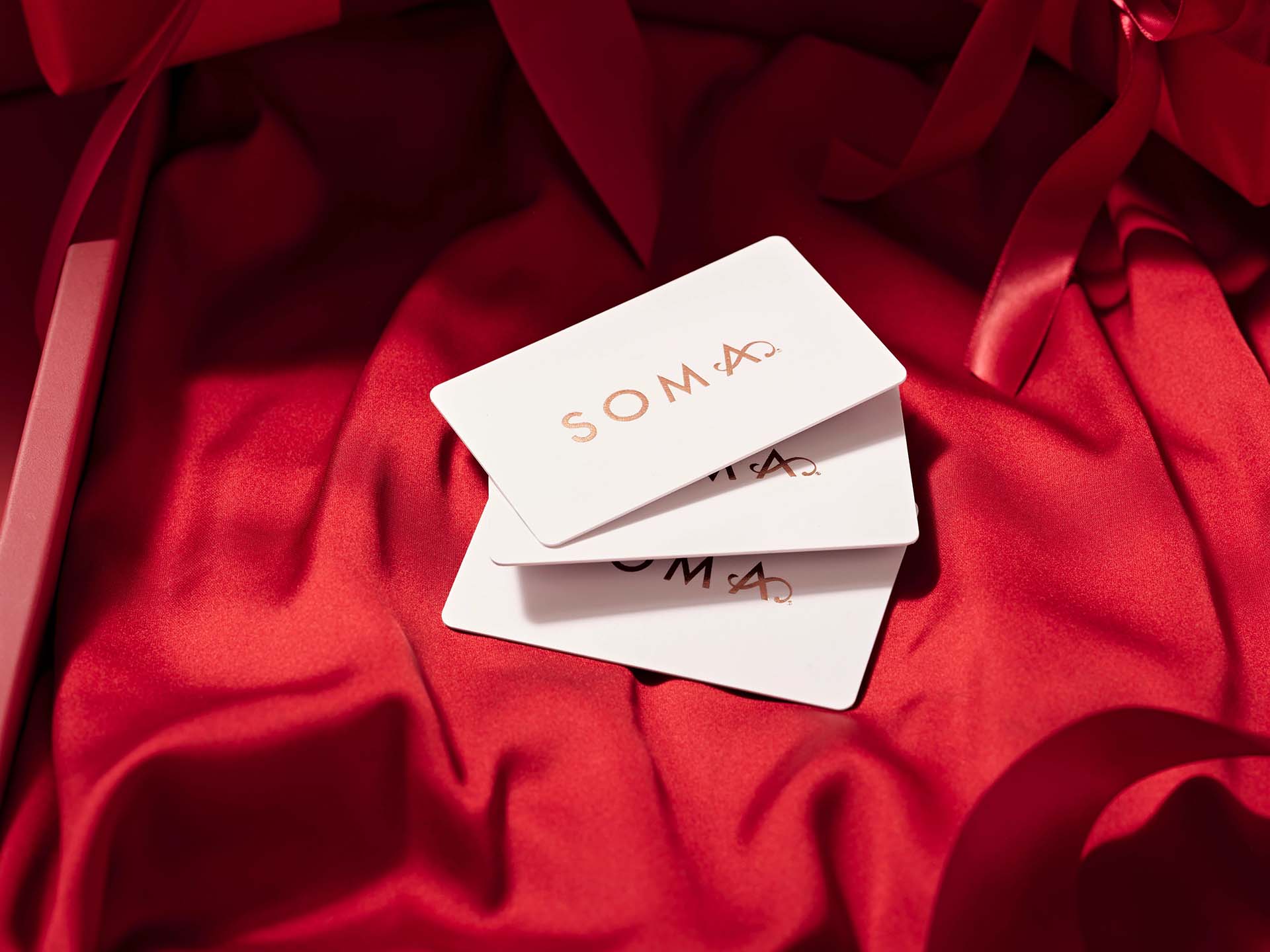 Soma<sup class=st-superscript>®</sup> laydown of red satin fabric with three Soma<sup class=st-superscript>®</sup> giftcards displayed in a fanned out pile.