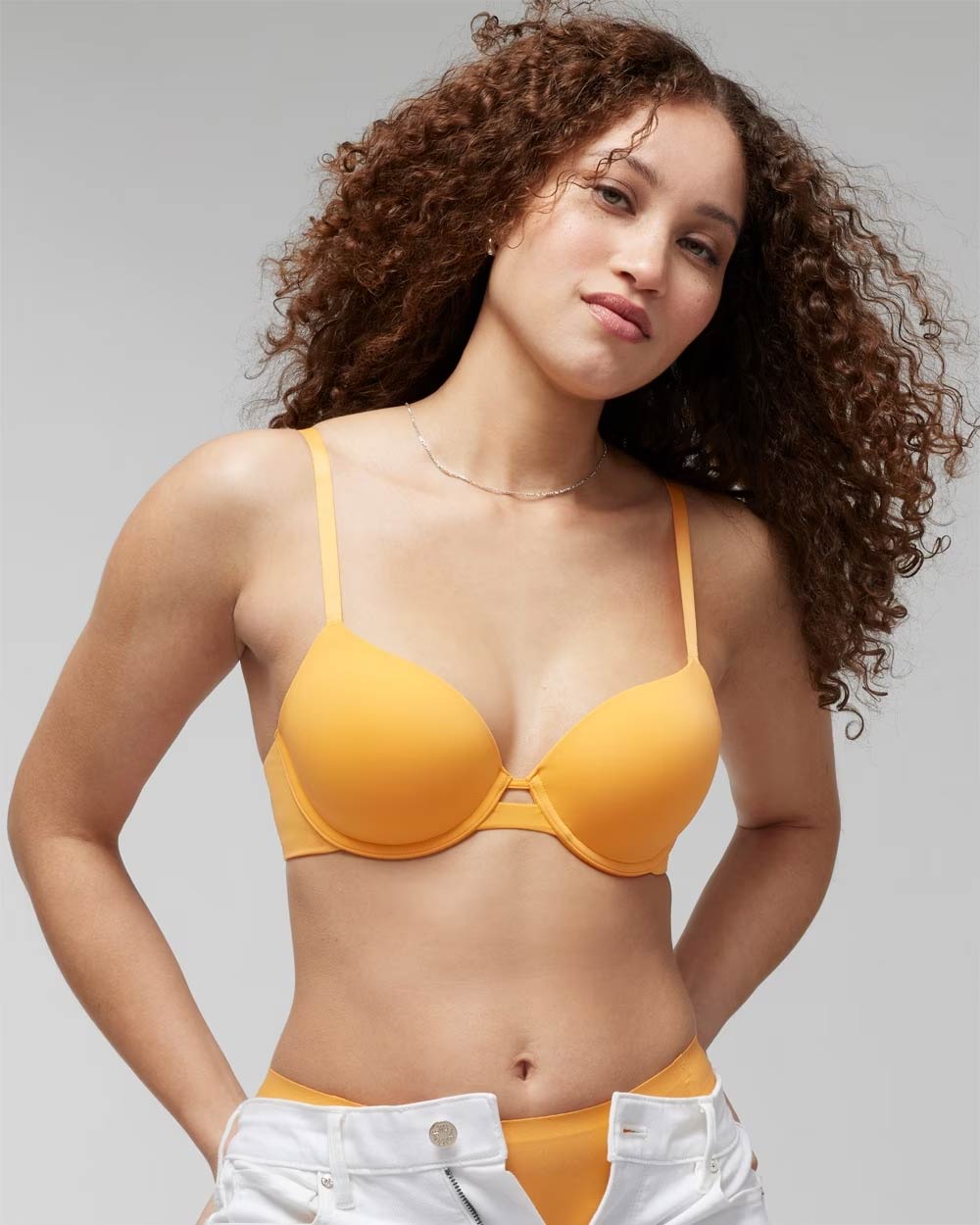 Soma<sup class=st-superscript>®</sup> women’s model wearing an orange bra with a sweetheart demi neckline, orange panties, and white shorts.