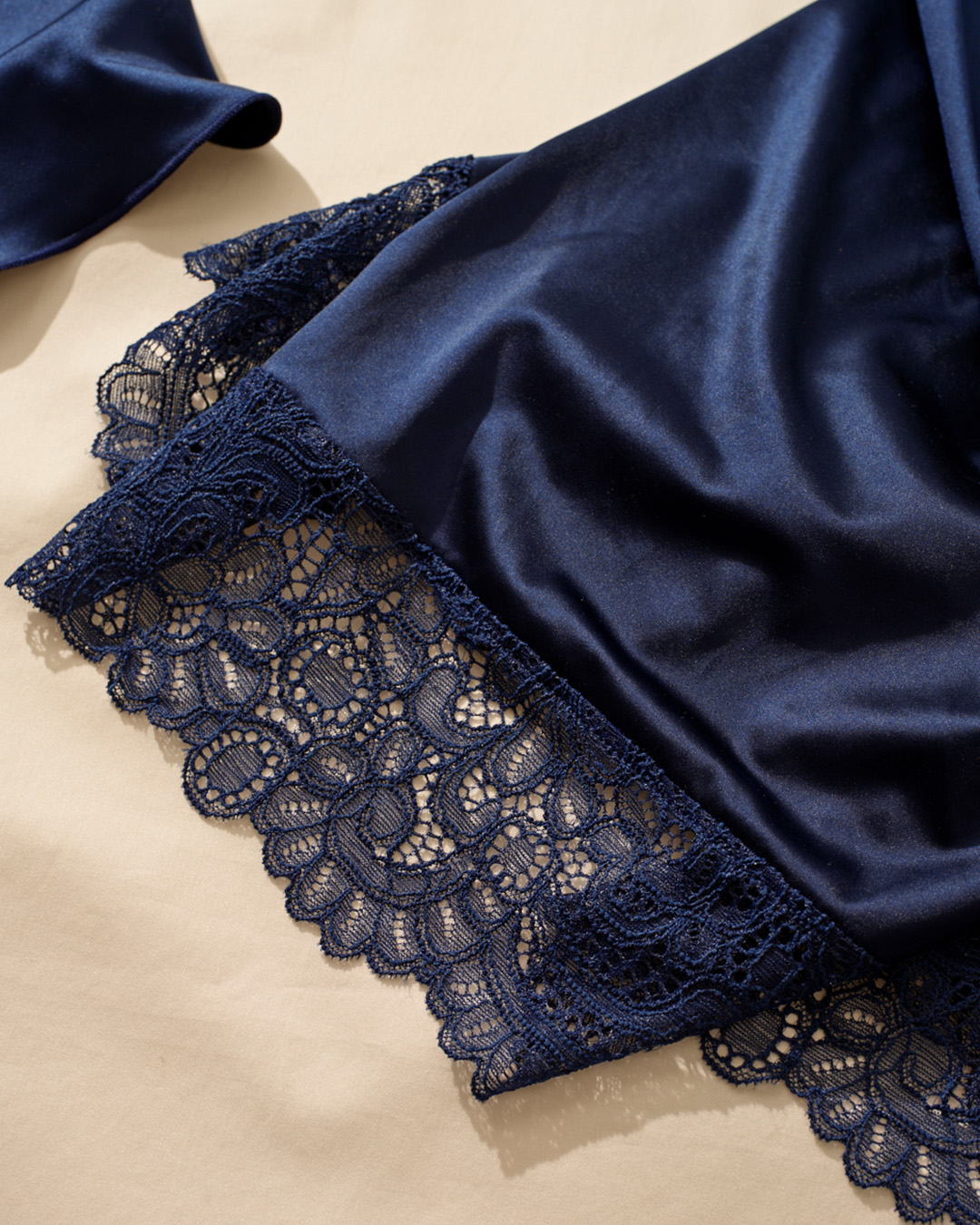 Close-up shot of laydown of navy lace-trimmed knit stretch satin chemise hem.