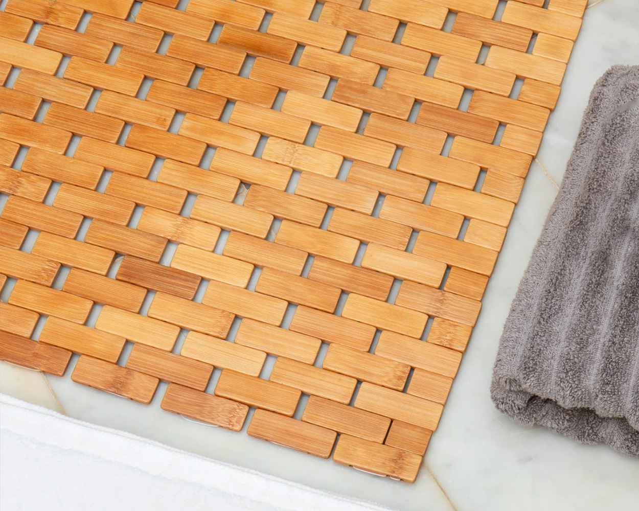Bamboo bath mat sitting on tile flower next to a grey folded towel.