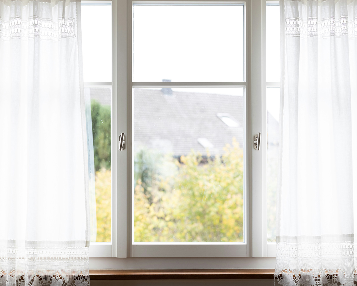 A view of a building and greenery through a window sill decorated with sheer white curtains.