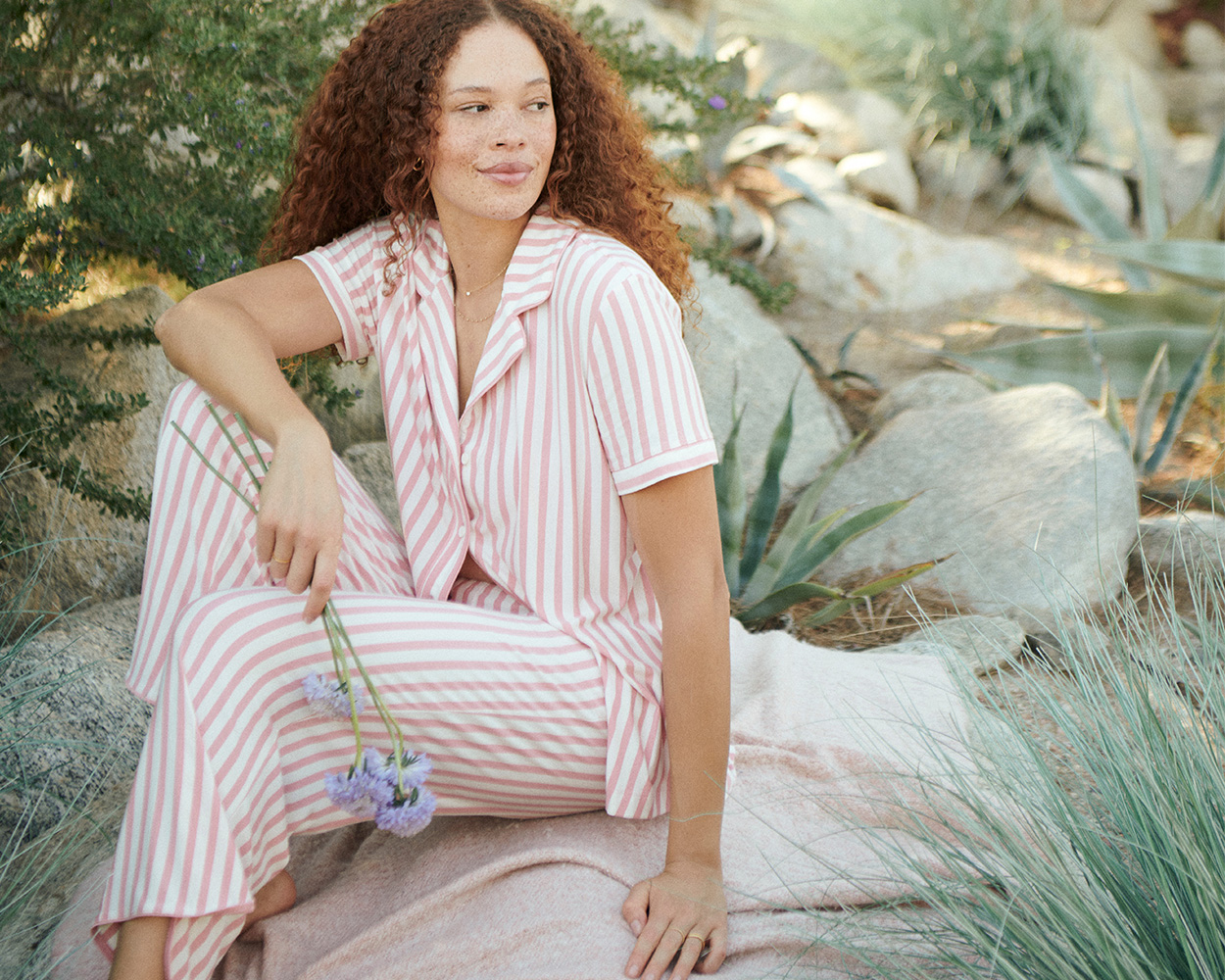 Soma<sup class=st-superscript>®</sup> model sitting on blanket outside, wearing a pink and white striped pajama set.